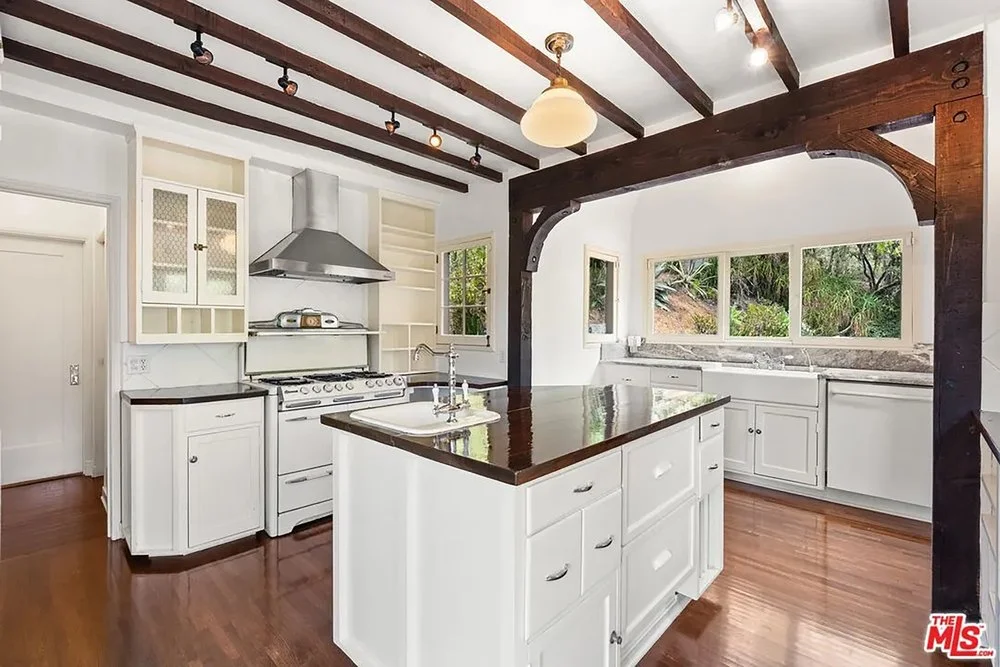 Spacious rustic kitchen with dark wood ceiling beams, white cabinetry, a large center island, and vintage-style white appliances.