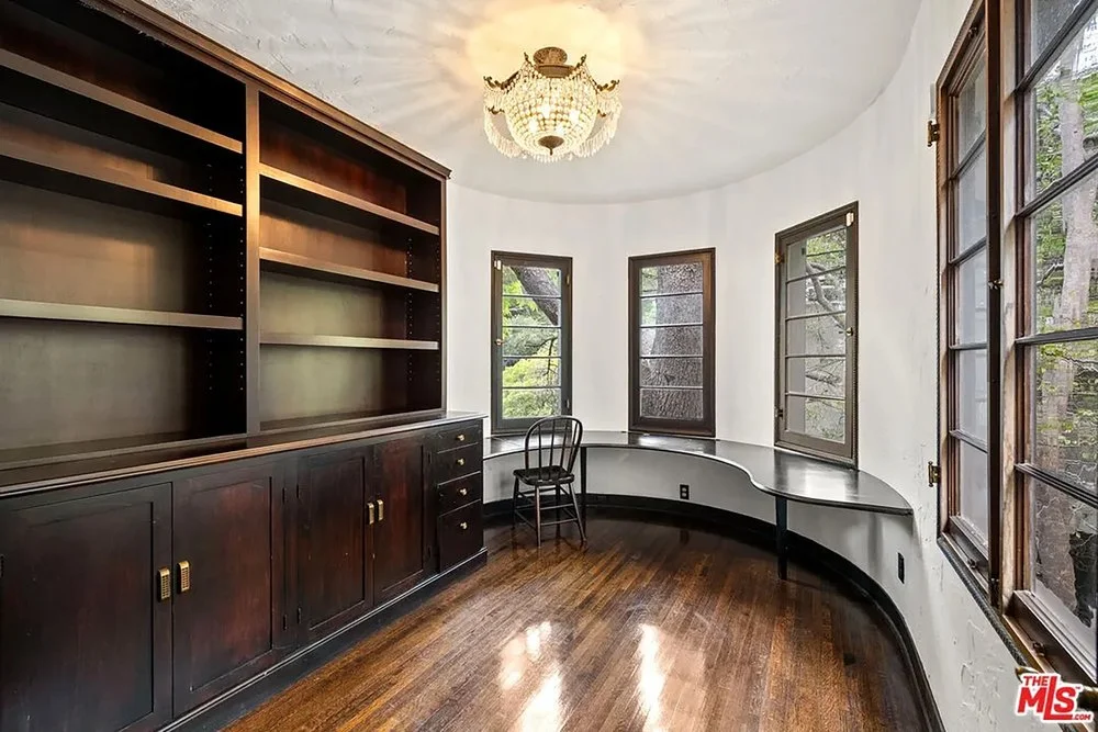 Curved home library space featuring a dark wood built-in bookcase, a integrated desk counter, and a crystal chandelier fixture.