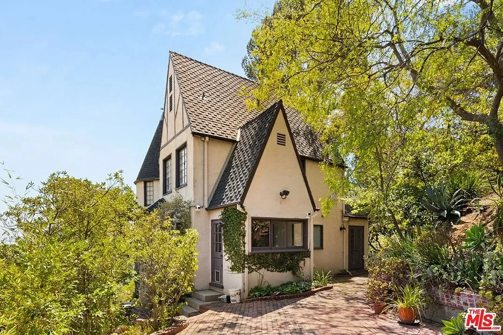 Storybook Tudor-style home set on a brick-paved driveway surrounded by lush trees and landscaping.